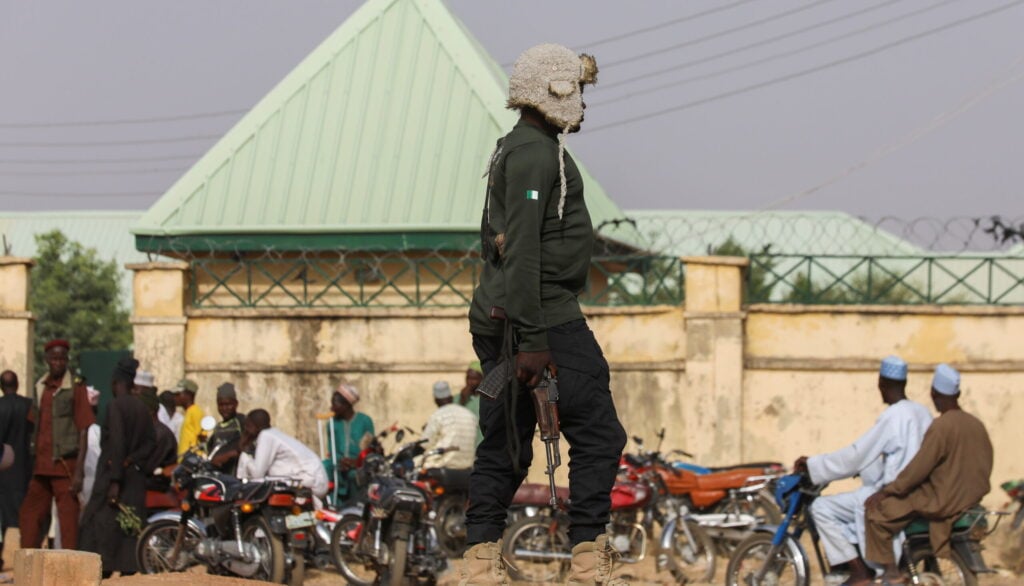 A member of the security forces holds a weapon as people wait for the arrival of the rescued JSS Jangebe schoolgirls in Jangebe, Zamfara, Nigeria